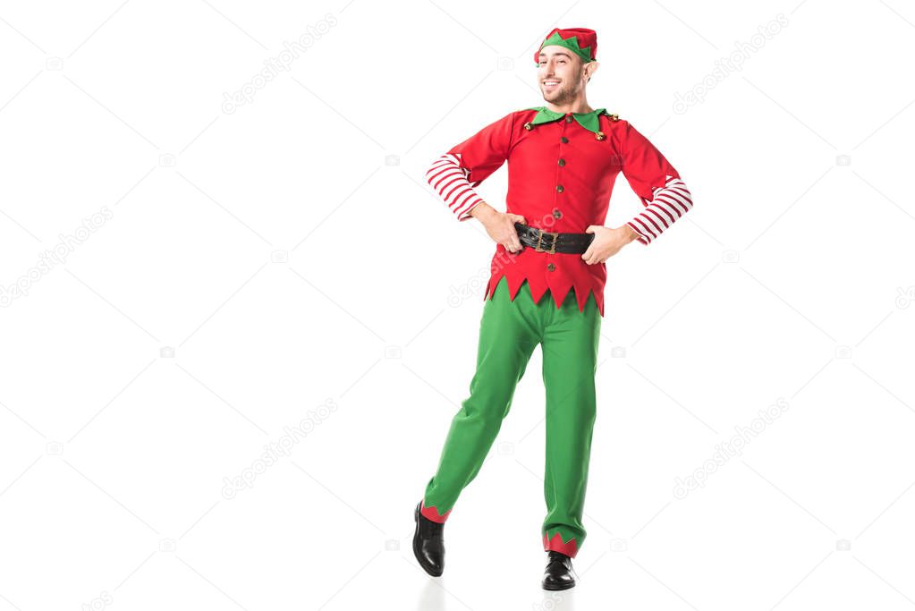 happy man in christmas elf costume looking at camera with hands on hips isolated on white