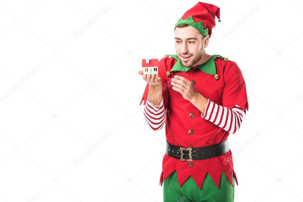 happy man in christmas elf costume holding house model isolated on white, real estate sale and insurance concept
