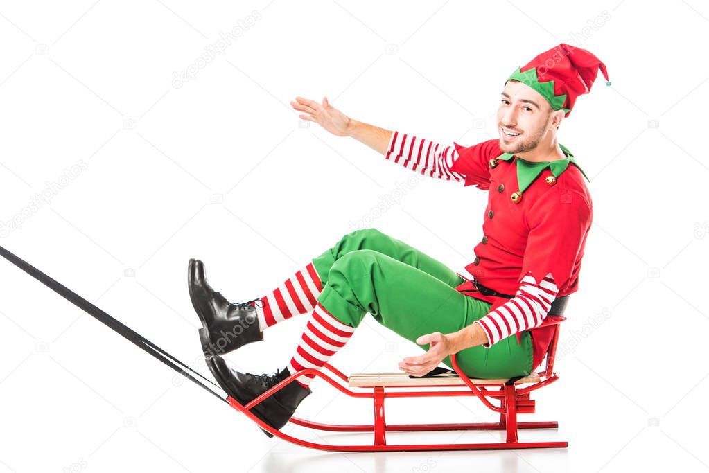 excited happy man in christmas elf costume riding sleigh and looking at camera isolated on white