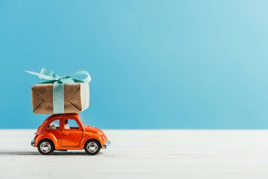 side view of toy red car with christmas gift box riding on white surface on blue background