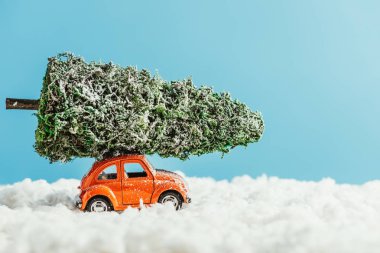 minyatür Noel ağacı ile oyuncak araç yan görünüm pamuk mavi zemin üzerine yapılan kar tarafından sürme çatı üzerinde