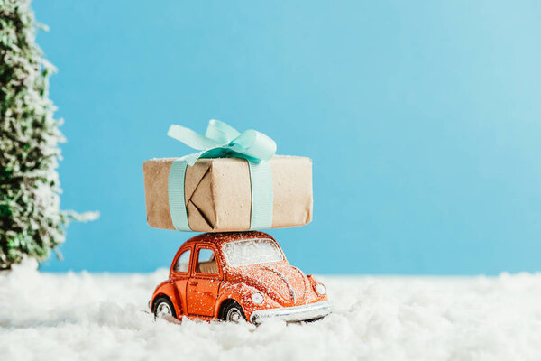 close-up shot of toy car with christmas gift box riding by snow made of cotton on blue background