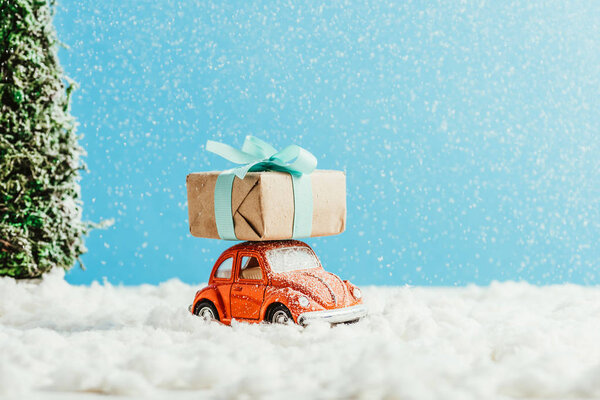 close-up shot of toy car with christmas present riding by snow made of cotton on blue background