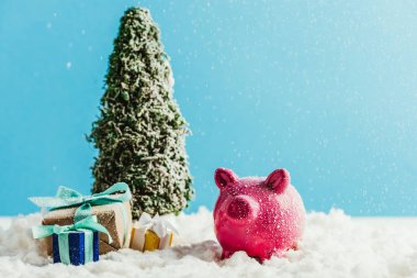 hediyeler ve kumbara ayakta kar üzerinde mavi arka plan ile minyatür Noel ağacı