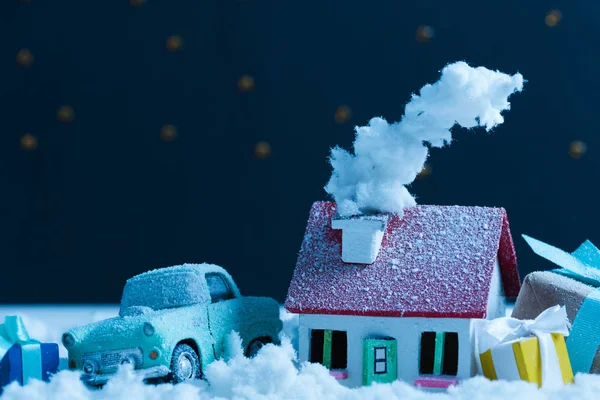 close-up shot of miniature car with christmas gifts and house covered with snow in night