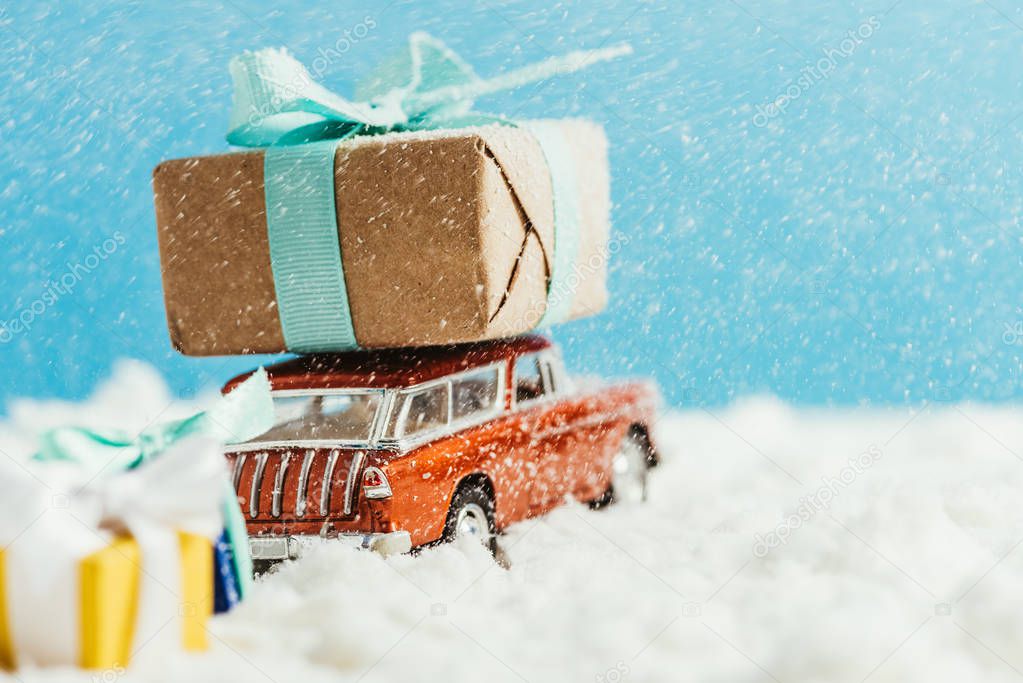 close-up shot of toy van with christmas gifts riding on snow on blue background