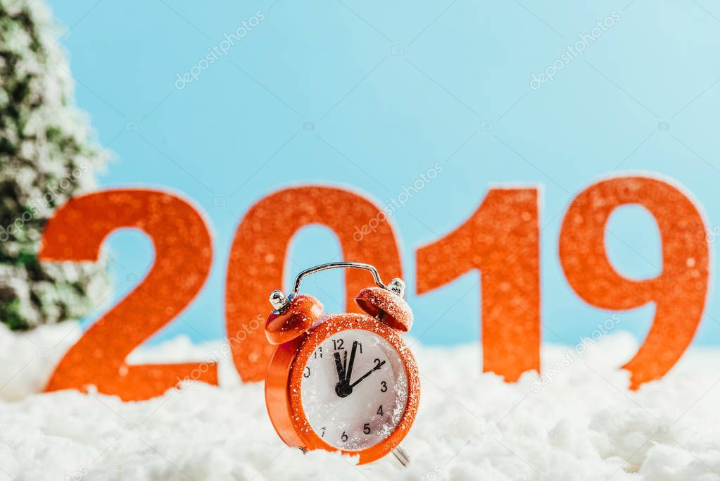 big red 2019 numbers with vintage alarm clock standing on snow on blue background, new year concept