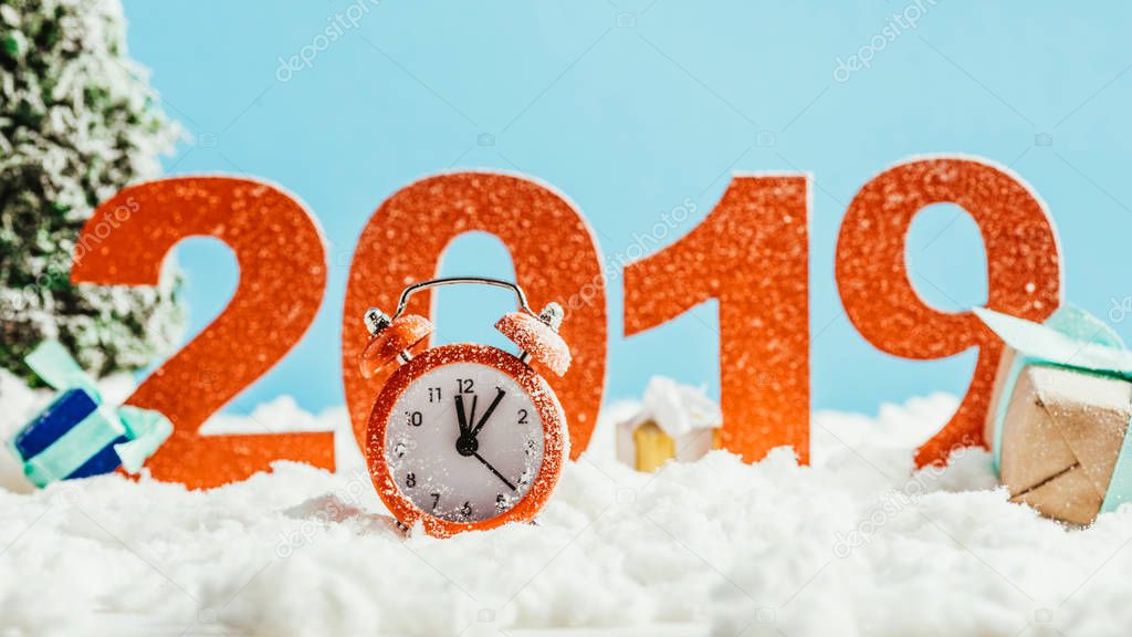 big red 2019 numbers with vintage alarm clock and gifts on snow on blue background, new year concept