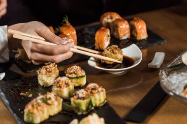 Partial view of woman dipping sushi in soy sauce with chopsticks clipart