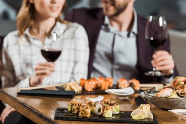 Partial view of couple eating sushi and drinking wine while having date in restaurant clipart