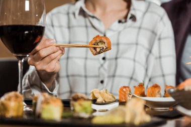 Partial view of woman eating sushi roll with chopsticks in restaurant clipart