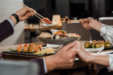 Çiftin birlikte suşi yerken elele kısmi görünümü restoranda rulo