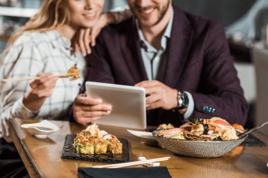 Suşi restoranında yemek yerken dijital aygıt kullanarak çiftin kırpılmış görünümü
