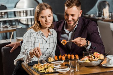 Mutlu genç yetişkin çift gülümseyen suşi yemek restoranda rulo 