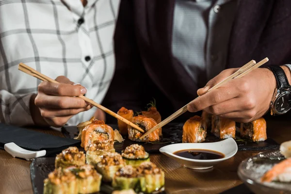 Partial view of people eating sushi rolls in restaurant