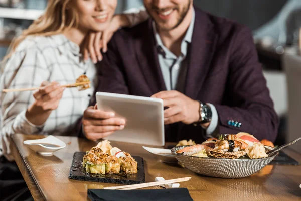 Vista Cortada Casal Usando Dispositivo Digital Enquanto Come Sushi Restaurante — Fotografia de Stock