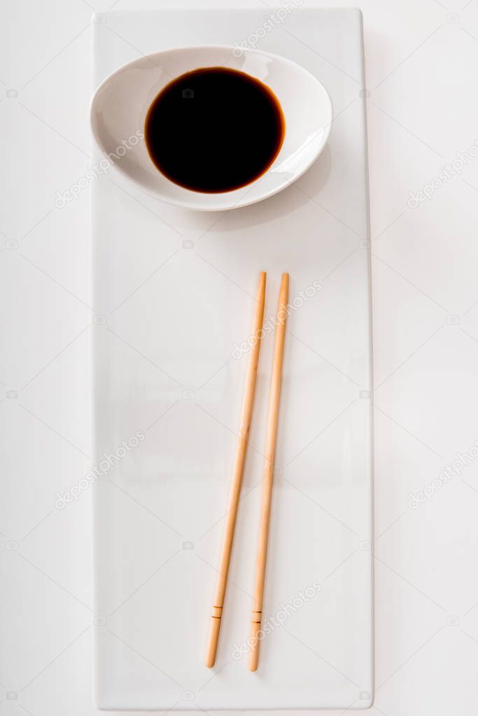 Top view of plate with soy sauce and chopsticks on white slate isolated on white