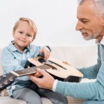 Foco seletivo de homem de meia idade ensinando neto tocando guitarra acústica em casa