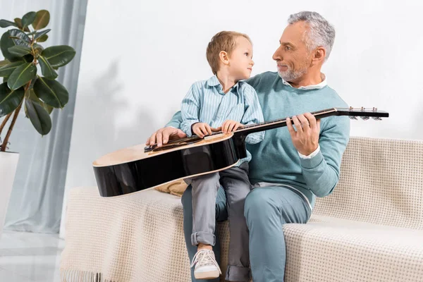 Zaskoczony Dziadek Gitara Akustyczna Ogląda Adorable Little Wnuka Kanapie Domu — Darmowe zdjęcie stockowe