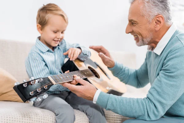 Счастливый Зрелый Мужчина Обучает Внука Играть Акустической Гитаре Дома — стоковое фото