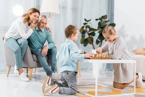 Crianças Sorrindo Jogando Xadrez Enquanto Seus Avós Sentados Perto Casa — Fotografia de Stock