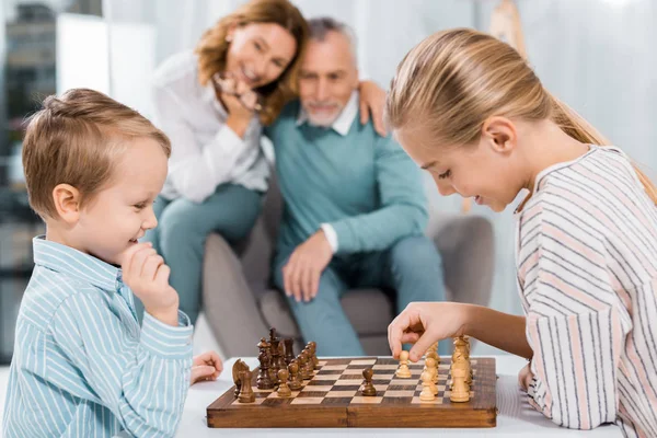 Vista Lateral Crianças Felizes Jogando Xadrez Enquanto Seus Avós Sentados — Fotografia de Stock