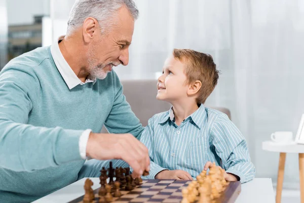 幸福的孙子和祖父一边在家里下棋的时候 一边看着对方的侧视图 — 图库照片