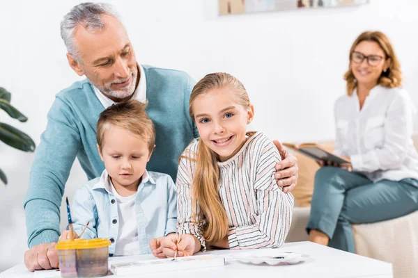 英俊的中年男子看如何孙子画 而他的妻子坐在后面的家 — 图库照片