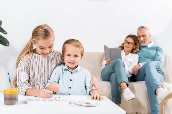 Sister Brother Painting Table While Grandparents Sitting Sofa Home — Stock Photo, Image