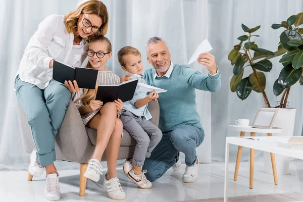 Grootouders Kleinkinderen Leerboeken Lezen Spelen Met Papier Vliegtuigen Sofa Thuis — Stockfoto