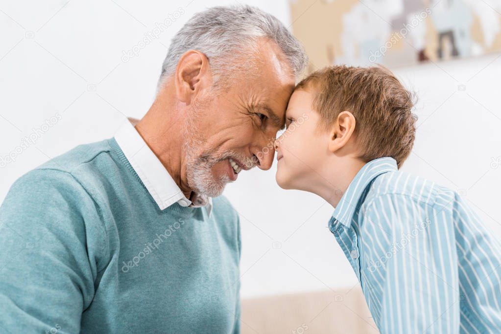 side view of happy middle aged man face to face with little grandson at home