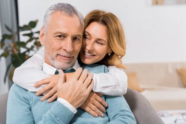 selective focus of happy attractive woman embracing middle aged husband at home clipart