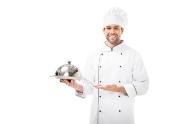 Servis tabağı kubbe ile tutarak ve üzerinde beyaz izole kamera bakarak mutlu genç şef