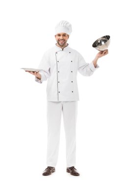smiling young chef taking of serving dome from plate and looking at camera isolated on white clipart