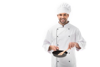 smiling young chef holding frying pan and wooden spatula isolated on white clipart