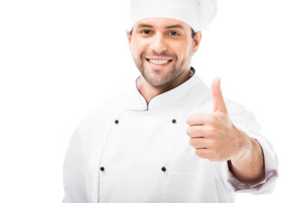 smiling young chef showing thumb up at camera isolated on white