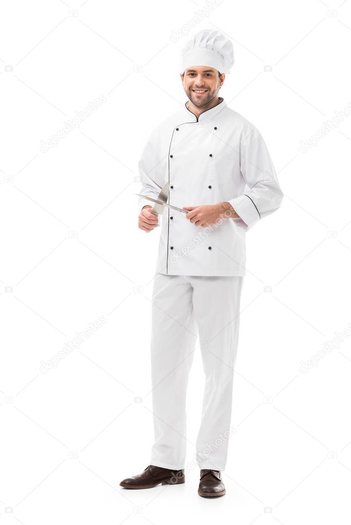 happy young chef holding cutting knives and looking at camera isolated on white