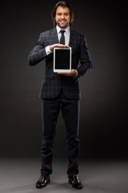 Dijital tablet boş ekran ile tutarak ve siyah kameraya gülümseyen yakışıklı genç işadamı