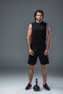 Kettlebell ile ayakta ve uzak gri görünümlü yakışıklı genç sporcu