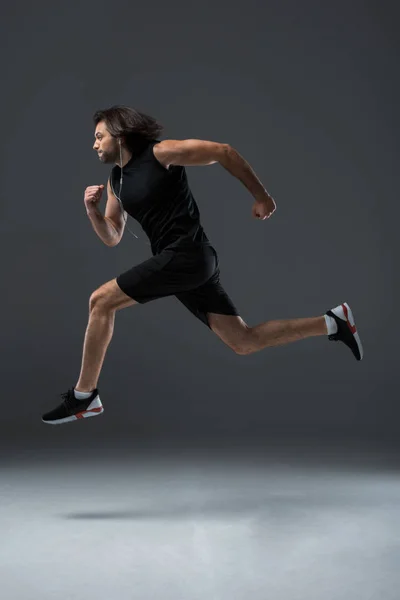 Zijaanzicht Van Atletische Man Oortelefoons Lopen Springen Grijs — Stockfoto