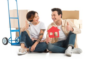 couple showing thumbs up signs and holding house model, moving to new house concept clipart