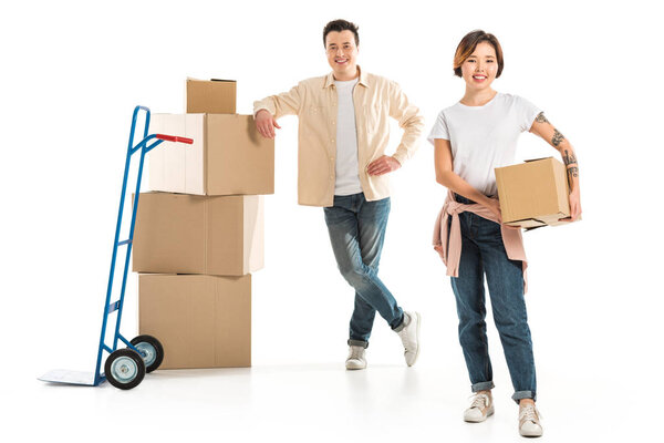 smiling couple looking at camera with cardboard boxes isolated on white, moving to new house concept