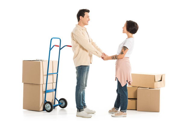 husband and wife holding hands with cardboard boxes on background, moving to new house concept