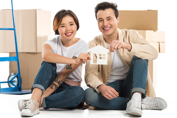 husband and wife holding house model with cardboard boxes on background, moving to new house concept