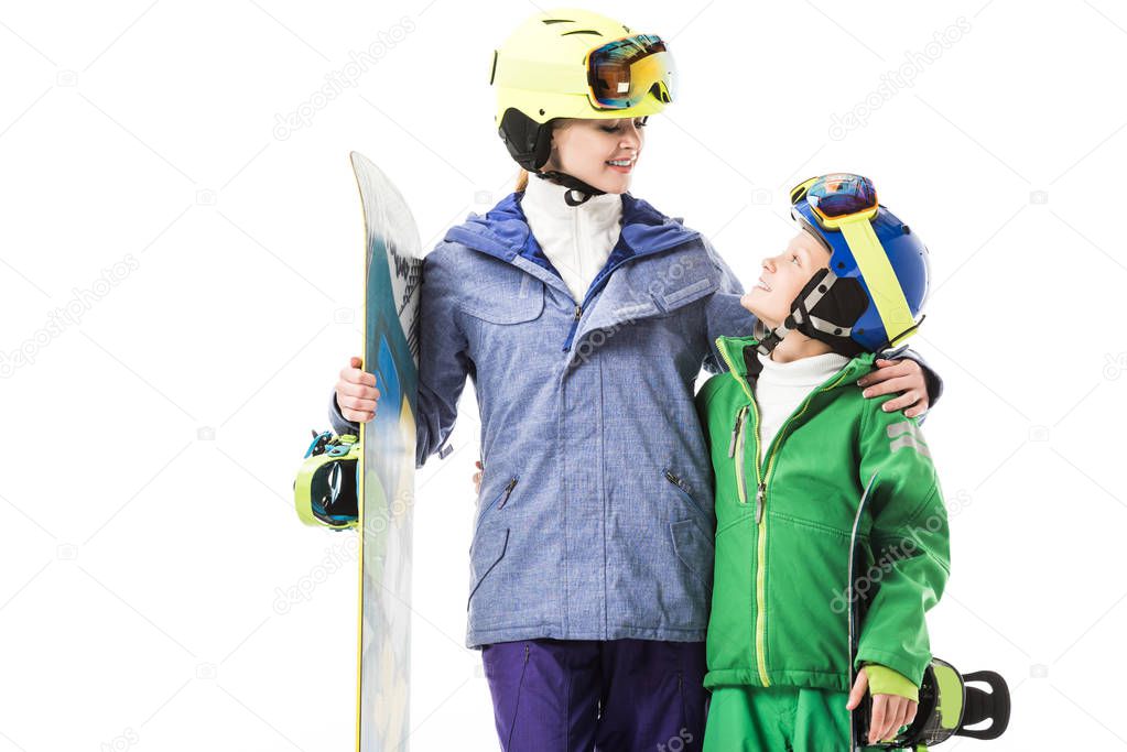 Smiling adult mother with snowboard hugging preteen son in snowsuit isolated on white