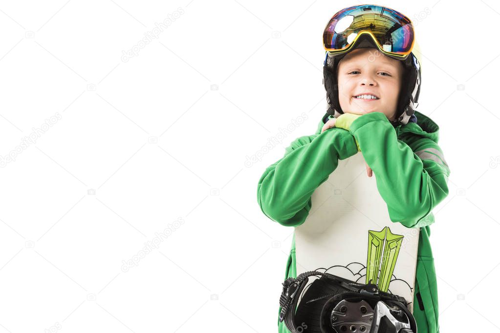 Cute preteen boy in ski suit and goggles leaning on white snowboard, smiling and looking at camera isolated on white