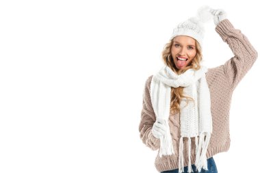 Bej örme kazak, beyaz şapka ve beyaz izole dil gösterilen eşarp neşeli genç kadın