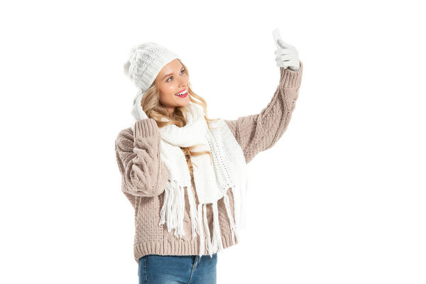 красивая молодая женщина в зимнем наряде делает селфи на смартфоне изолированы на белом
