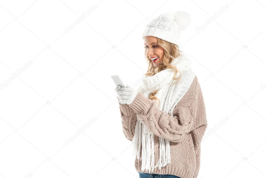 beautiful smiling woman in winter hat and scarf using smartphone isolated on white