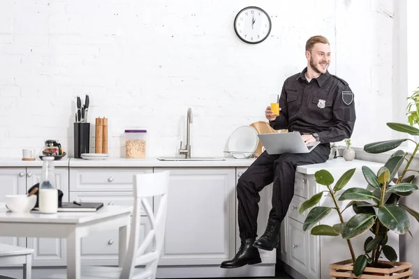 Sorrindo Homem Uniforme Policial Sentado Mesa Cozinha Bebendo Suco Laranja — Fotografia de Stock Grátis